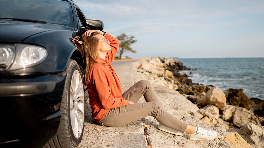 Mujer apoyada en coche de alquiler con vista a la playa en Costa Rica